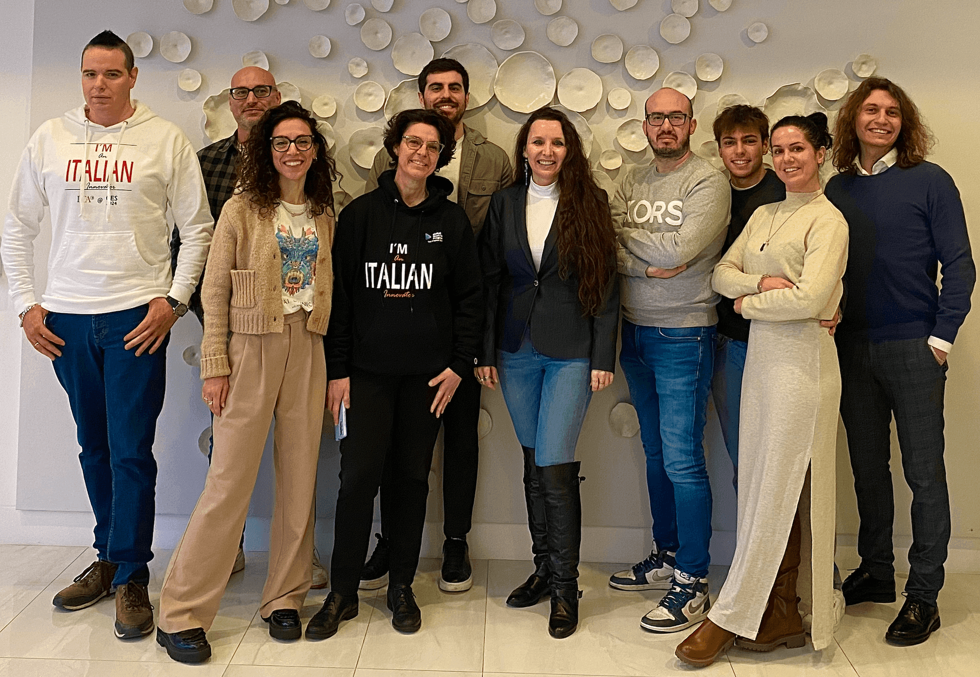 Group of ten people standing together indoors, posing for a photo with a wall art background.